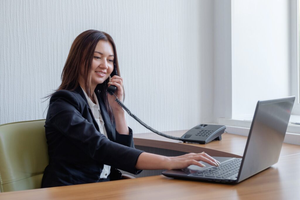 A businesswoman is working on her laptop and talking on the phone